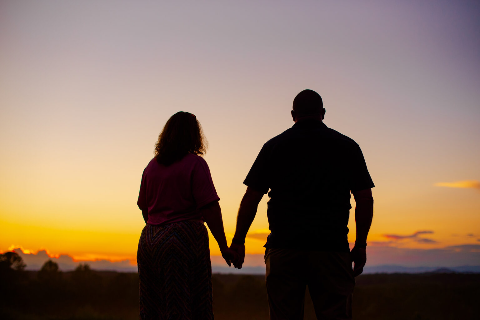 Couple holding hands at sunset, symbolizing caregiver wellness and community.